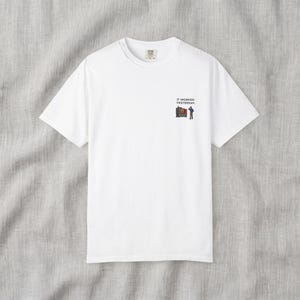 Pode incluir: Uma t-shirt branca de manga curta com um pequeno gráfico no lado esquerdo do peito. O gráfico mostra uma pessoa de pé ao lado de uma máquina com o texto IT WORKED YESTERDAY impresso em letras maiúsculas pretas acima da ilustração.