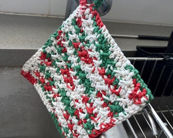 Peut inclure: Un manique carré crocheté à la main présentant un motif varié de fils rouge, vert forêt et blanc cassé. L'article possède une petite boucle intégrée à un coin pour le suspendre et un point texturé dense sur tout le tissu.