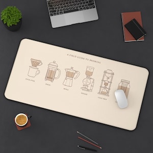 May include: A rectangular desk mat with a cream-colored surface featuring the text A FIELD GUIDE TO BREWING and line art illustrations of coffee makers including pour over, press, moka, siphon, cold drip, and cold brew methods.