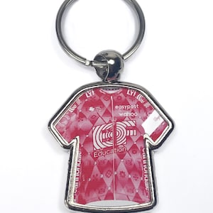 May include: A silver metal keychain shaped like a cycling jersey. The jersey is pink with a white diamond pattern and features the text "easypost wahoo Education Cannondale LYI!"