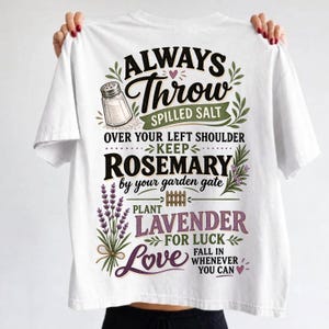 以下が含まれることがあります： ALWAYS THROW SPILLED SALT OVER YOUR LEFT SHOULDER KEEP ROSEMARY BY YOUR GARDEN GATE PLANT LAVENDER FOR LUCK LOVE FALL IN WHENEVER YOU CANというテキストと塩のイラストがプリントされた白いTシャツ。