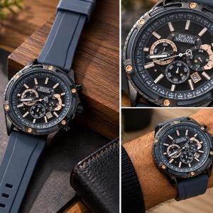 Op de afbeelding: Een Dylan Valentin chronograaf horloge met een donkerblauwe siliconen band en een zwarte wijzerplaat. Het horloge heeft roségoudkleurige accenten op de ring, wijzers en sub-wijzerplaten, met een datumvenster op de vier-uur-positie.