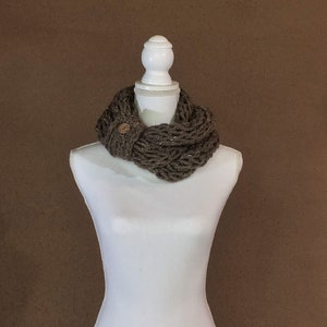 May include: A brown knitted infinity scarf with a wooden button. The scarf is displayed on a white mannequin.