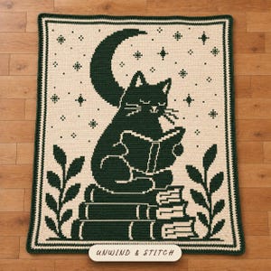 May include: A rectangular crochet blanket featuring a dark green design on a cream background. The pattern depicts a cat reading a book while sitting on a stack of books under a crescent moon and stars, with leafy branches on the sides. Text reads UNWIND & STITCH.