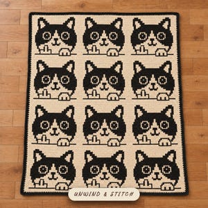 May include: A rectangular crochet blanket featuring a repeating pattern of twelve black and white cat faces arranged in a grid. Each cat is depicted with a raised middle finger. The blanket has a dark border and the text UNWIND & STITCH at the bottom.