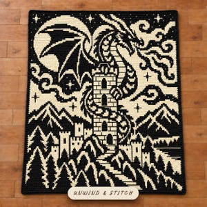 May include: A rectangular crochet blanket featuring a black and cream tapestry design of a dragon coiled around a tall stone tower. The scene includes mountains, a forest, and a starry night sky. The text UNWIND & STITCH is printed at the bottom.
