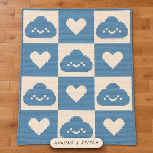 May include: A rectangular crochet blanket featuring a checkered pattern of light blue and cream squares. The design alternates between blue smiling cloud icons and cream-colored hearts. The text UNWIND & STITCH is printed on a label.