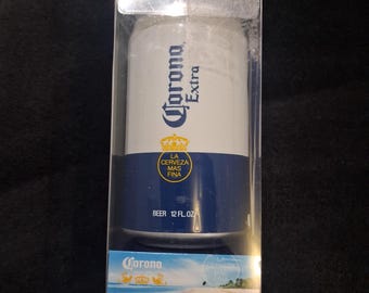 May include: A Corona Extra branded true wireless can speaker packaged in a clear plastic box. The speaker is white and blue with the text Corona Extra, La Cerveza Mas Fina, and Beer 12 fl. oz. The packaging includes a Bluetooth logo.