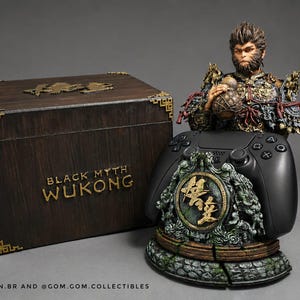 Puede incluir: Una caja de madera oscura con detalles dorados en las esquinas y el texto Black Myth Wukong, junto a una figura detallada de un guerrero mono con una calabaza, sobre una base decorativa que sostiene un mando de juego negro con texto dorado.