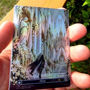 May include: A rectangular trading card featuring a detailed illustration of a figure in a dark cloak walking through a white gothic cathedral with angel statues and floral arrangements. The bottom black border displays the text Plains, P 001 Vampyr Land Series, and PXY-EN TESLA XIII.