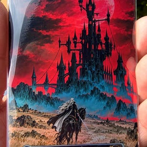 May include: A rectangular trading card featuring a dark castle silhouette against a vibrant red sky. A figure with long white hair rides a black horse in the foreground. The card displays the text Mountain, P 002 Vampyr Land Series, PXY-EN TESLA XIII.