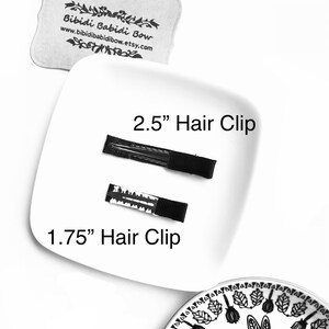 Op de afbeelding: Twee zwarte haarclips op een wit bord. De grotere clip is 2,5 inch lang en de kleinere clip is 1,75 inch lang.