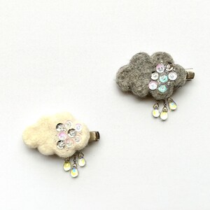 May include: Two felt cloud hair clips with silver glitter and iridescent raindrop charms. One cloud is gray and the other is white.