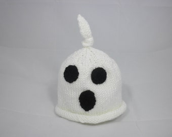 May include: A white knitted ghost hat with three black facial features: two round eyes and a large oval mouth. The hat has a knotted top and a ribbed brim. This Halloween-themed hat is perfect for costumes.