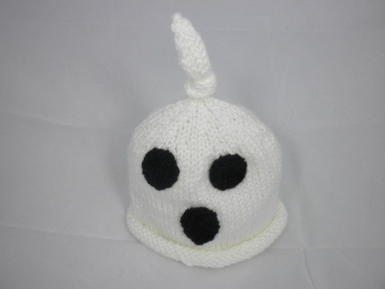 Puede incluir: Un gorro de fantasma blanco tejido con tres agujeros negros para los ojos y una boca negra. El gorro tiene una parte superior anudada y un borde enrollado. Este gorro hecho a mano es perfecto para Halloween o fiestas de disfraces.