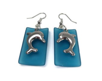 Silver Dolphin Earrings Against Curved Blue Glass
