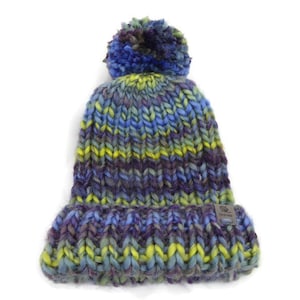 Puede incluir: Un gorro de punto grueso en tonos azules, morados y amarillos con un gran pompón en la parte superior. El gorro tiene un borde doblado y una pequeña etiqueta. Este gorro cálido es perfecto para el frío.