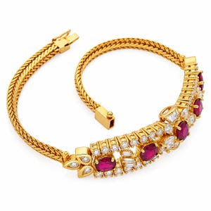 Könnte beinhalten: Ein goldenes Armband mit geflochtenem Kettenmuster und einem zentralen Dekorelement. Das Mittelstück ist mit oval geschliffenen roten Rubinen sowie runden und im Baguetteschliff facettierten klaren Steinen in Gold gefasst und hat einen Kastenverschluss.