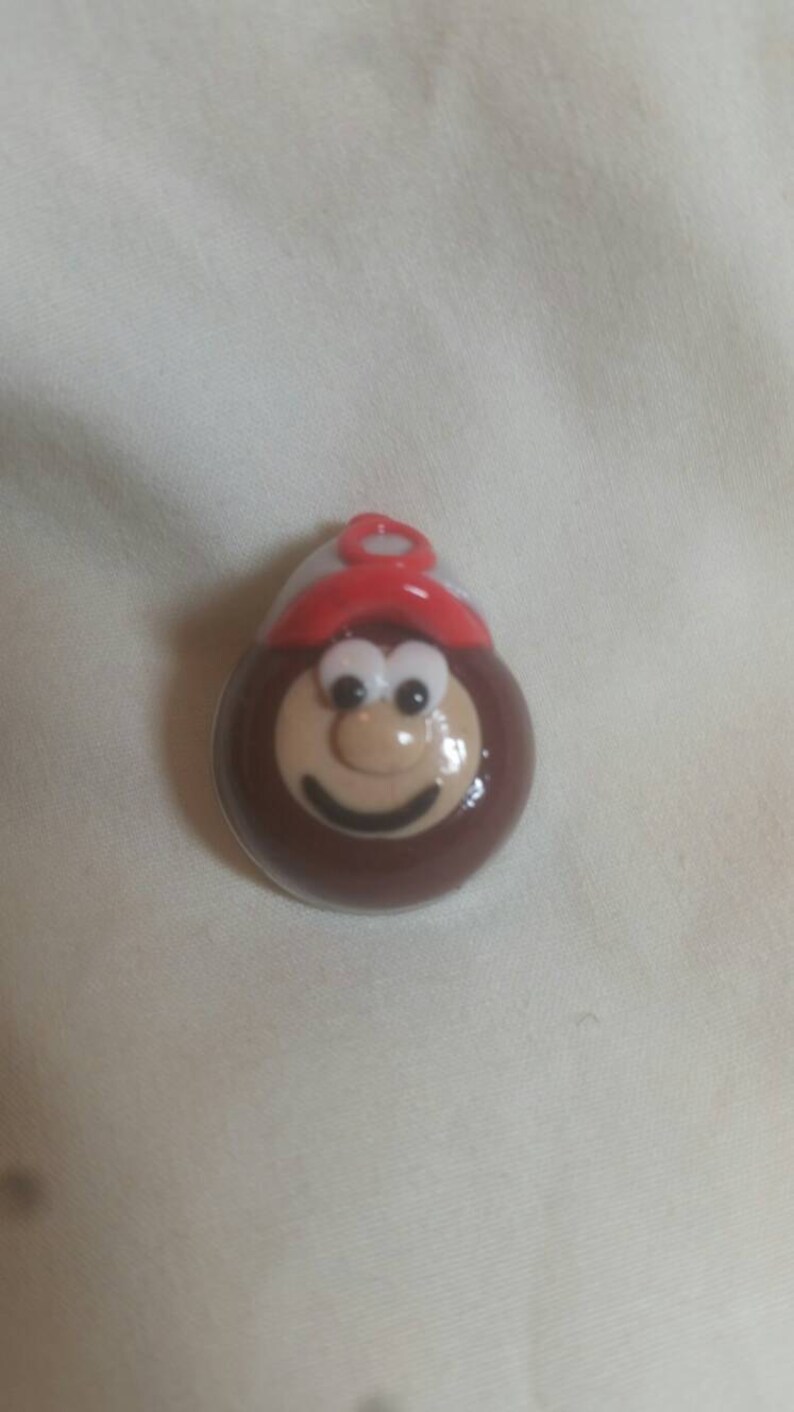 May include: A brown, cartoon-like character with a smiling face, large eyes, and a red hat. The character is round and has a light tan face with a dark brown outline. The hat is red with a white band.