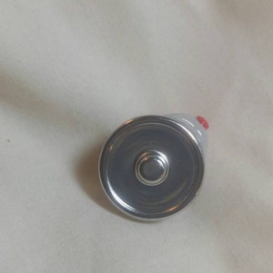 May include: A small, gray ceramic mouse-shaped bottle stopper with a silver metal base. The mouse has a red nose and is viewed from above. The stopper is designed to fit into a bottle.