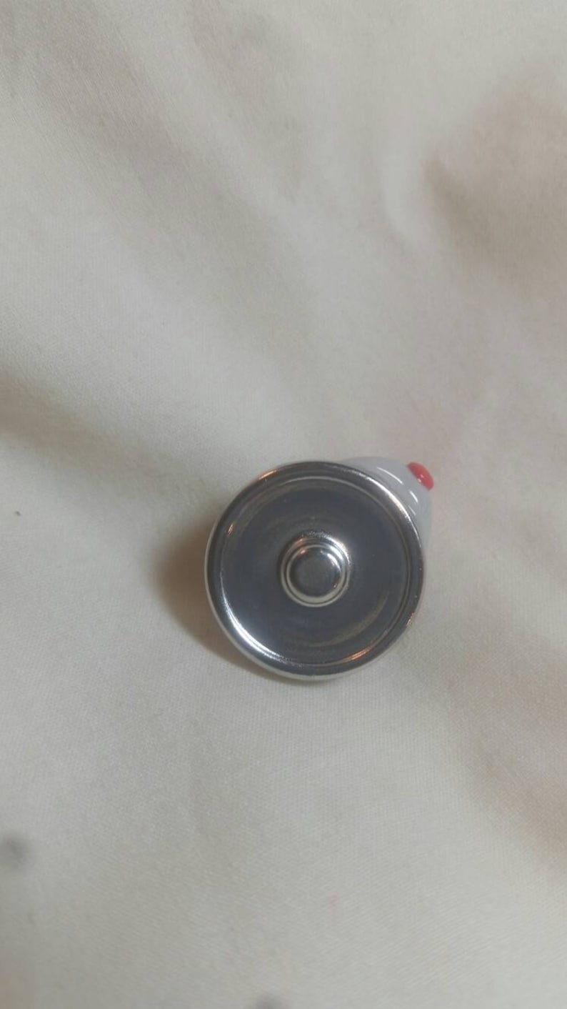 May include: A small, gray ceramic mouse-shaped bottle stopper with a silver metal base. The mouse has a red nose and is viewed from above. The stopper is designed to fit into a bottle.