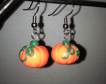 May include: A pair of silver pumpkin earrings with green stems and leaves. The pumpkins are orange and have a glossy finish.
