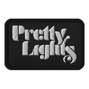 May include: A black rectangular patch with the embroidered text "Pretty Lights" in white. The text is in a stylized, vintage font. The patch has a black border.