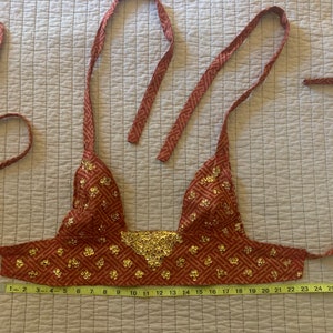 May include: A red and gold sequined halter top with a geometric pattern. The top has adjustable straps and a tie closure at the back. The top is 14 inches wide and 12 inches long.