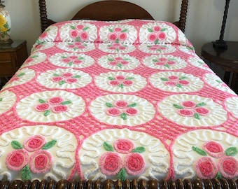 May include: A pink and white bedspread with a floral pattern. The bedspread is made of a soft, fluffy material and features a repeating design of pink roses with green leaves.