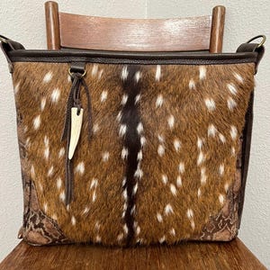 May include: A brown leather shoulder bag with a spotted pattern. The bag has a long strap and a small bone charm.