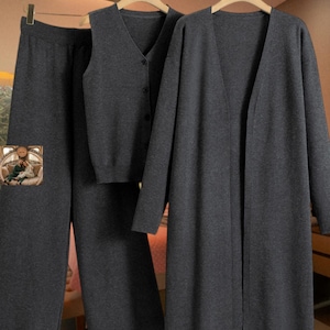 Peut inclure: Un ensemble en tricot gris anthracite composé d'un pantalon large, d'un gilet sans manches à col en V boutonné et d'un cardigan à manches longues ouvert sur le devant. Les vêtements présentent une couleur gris foncé et une texture uniforme.