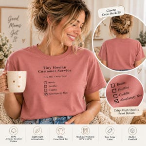 Peut inclure: Un t-shirt à col rond rose poudré avec un texte noir indiquant Tiny Human Customer Service, How May I Help You? et une liste à cocher comprenant Bottle, Pacifier, Cuddle, avec la case Absolutely Not cochée. Le t-shirt a des manches courtes.