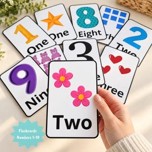May include: A set of educational flashcards featuring numbers 1 through 10, each displaying a large numeral, the corresponding written word, and a matching quantity of colorful illustrations such as stars, bears, hearts, and flowers.