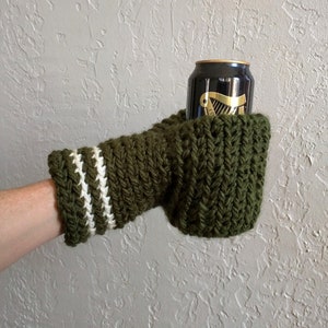 This beer mitten is green with white stripes around the wrist. It is part crochet can holder part mitten. A hand is in it and a can of beer inside the holder. The bottom is covered so the can stays in place. It can be used on either hand.