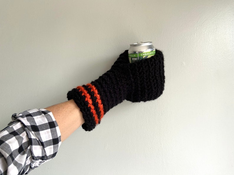This beer mitten is black with orange gold stripes around the wrist. It is part crochet can holder part mitten. A hand is in it and a can of beer inside the holder. The bottom is covered so the can stays in place. It can be used on either hand.