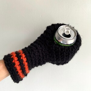 This beer mitten is black with orange gold stripes around the wrist. It is part crochet can holder part mitten. A hand is in it and a can of beer inside the holder. The bottom is covered so the can stays in place. It can be used on either hand.