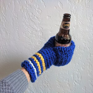 This beer mitten is blue with white and yellow stripes around the wrist. It is part crochet can holder part mitten. A hand is in it and a can of beer inside the holder. The bottom is covered so the can stays in place. It can be used on either hand.