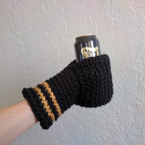 This beer mitten is black with gold stripes around the wrist. It is part crochet can holder part mitten. A hand is in it and a can of beer inside the holder. The bottom is covered so the can stays in place. It can be used on either hand.