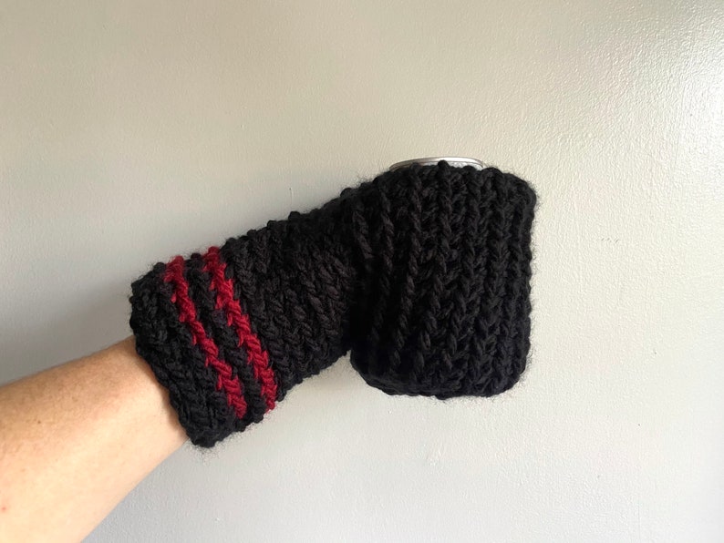 This beer mitten is black with red stripes around the wrist. It is part crochet can holder part mitten. A hand is in it and a can of beer inside the holder. The bottom is covered so the can stays in place. It can be used on either hand.