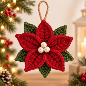 May include: A crocheted poinsettia ornament featuring vibrant red petals and dark green leaves arranged in a star shape. Three small, cream-colored crocheted spheres are centered in the middle. A tan twisted rope loop is attached to the top for hanging.