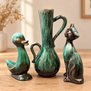 May include: A set of three ceramic decorative objects featuring a duck figurine, a tall vase with two handles, and a cat figurine. Each piece has a glossy finish with a blended colour palette of deep forest green, teal, and dark brown tones.