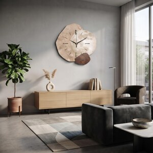 May include: A wall clock featuring an irregular, layered design with a large, light-toned, organic-shaped base, a circular centre element, and a smaller dark brown accent piece. It has thin black hands and simple black hour markers.