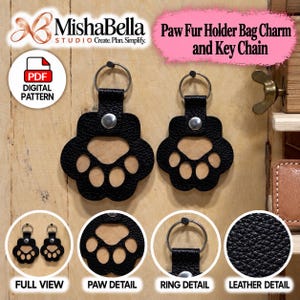 May include: Two black textured paw-shaped keychains with silver metal rings and snaps. The design features a central pad and four toe cutouts. Text includes MishaBella Studio, Paw Fur Holder Bag Charm and Key Chain, and PDF Digital Pattern.