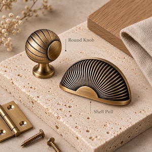 Op de afbeelding: Een ronde knop van messingkleurig metaal met een geribbelde textuur en een bijpassende halfronde schelpvormige greep met een stralend ribbelpatroon. De set bevat een plat rechthoekig scharnier en twee kleine metalen schroeven met antieke afwerking.