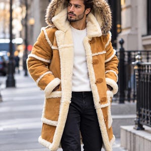 Puede incluir: Un abrigo de ante color tostado con forro y ribetes de piel de oveja color crema. El abrigo cuenta con una capucha grande con borde de piel sintética, mangas largas y un cierre frontal con botones de madera tipo trenca sobre camisa y pantalón.