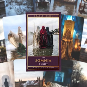 May include: A tarot card deck titled "The Somnia Tarot" by Nicolas Bruno, with a dark purple and gold design. The card features figures in hooded cloaks holding swords, standing in water. Other cards with similar imagery are in the background.