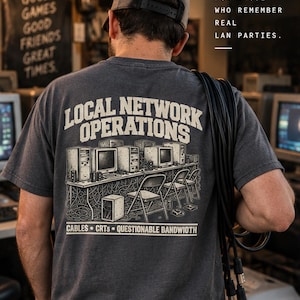 May include: A dark gray t-shirt featuring a back graphic of a LAN party setup with computers, cables, and chairs. The text reads: LOCAL NETWORK OPERATIONS, CABLES • CRTS • QUESTIONABLE BANDWIDTH, and FOR THOSE WHO REMEMBER REAL LAN PARTIES.
