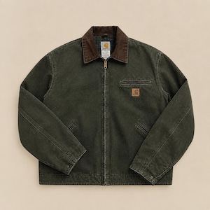 May include: A dark olive green canvas jacket featuring a brown corduroy collar, a full-length front zip, and two lower welt pockets. A small rectangular Carhartt brand patch is stitched onto the left chest pocket area of the garment.