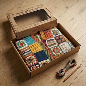 Könnte beinhalten: Eine mehrfarbige Patchwork-Häkelstrickjacke mit verschiedenen quadratischen Mustern in Blau-, Gelb-, Orange- und Weißtönen, verpackt in einem Karton mit der Aufschrift Artisan Stitches Patchwork Grandeur Cardigan, inklusive Garnstrang und Holzhäkelnadel.