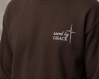 Sudadera cristiana estética, cuello redondo bordado con la frase "Salvados por la Gracia", jersey minimalista de fe, suéter con versículo bíblico, estilo urbano moderno con Jesús.